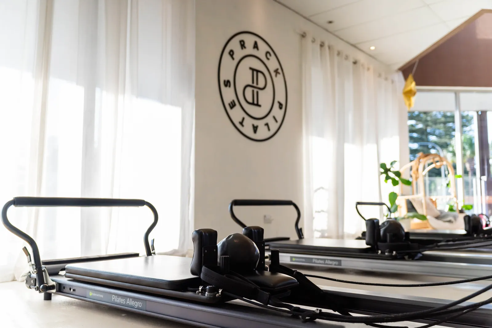 Two reformers set up side by side beneath the Prack Pilates roundel painted on the studio wall