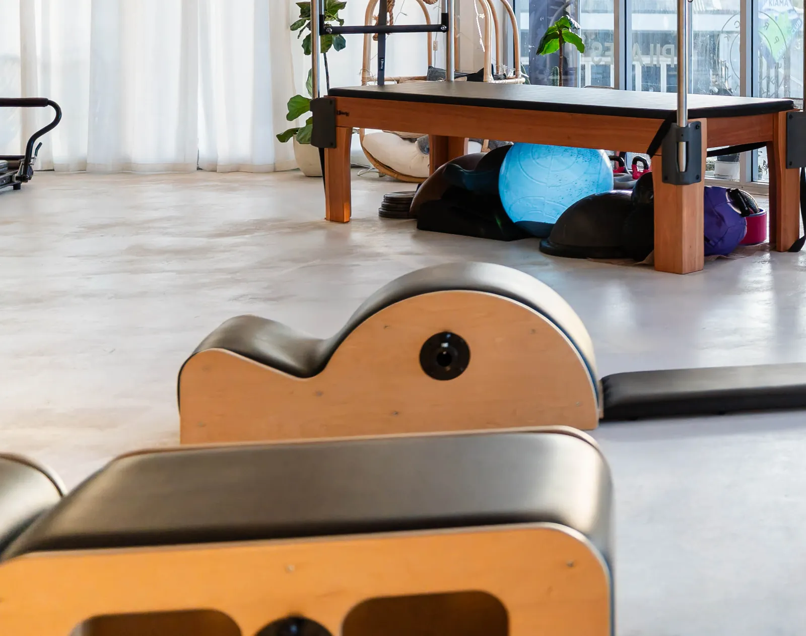 Two timber spine correctors on the studio floor, with the Cadillac and a rack of exercise balls behind them