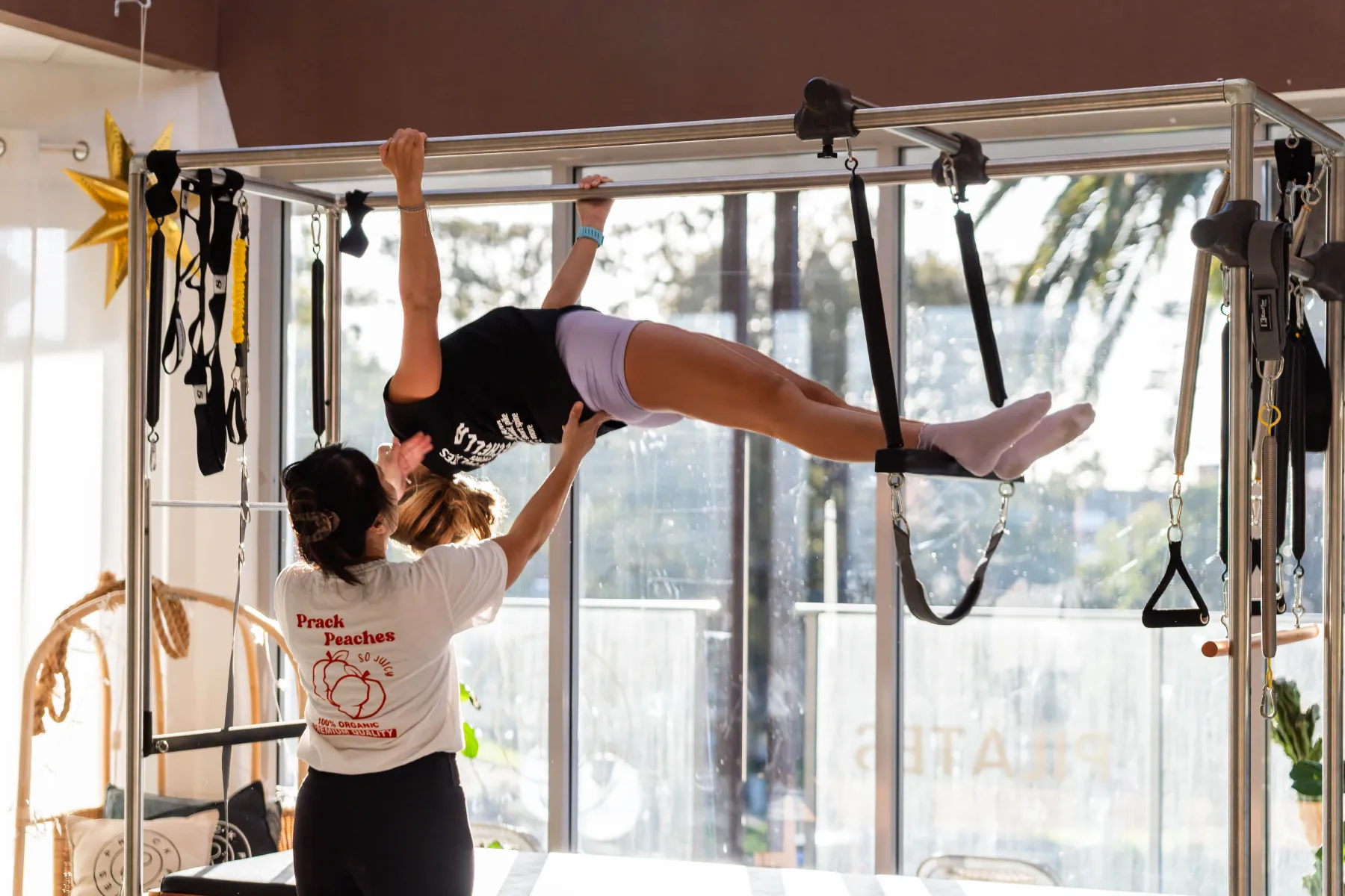 An instructor supporting one client through a movement on the Cadillac at Prack Pilates in Kiama
