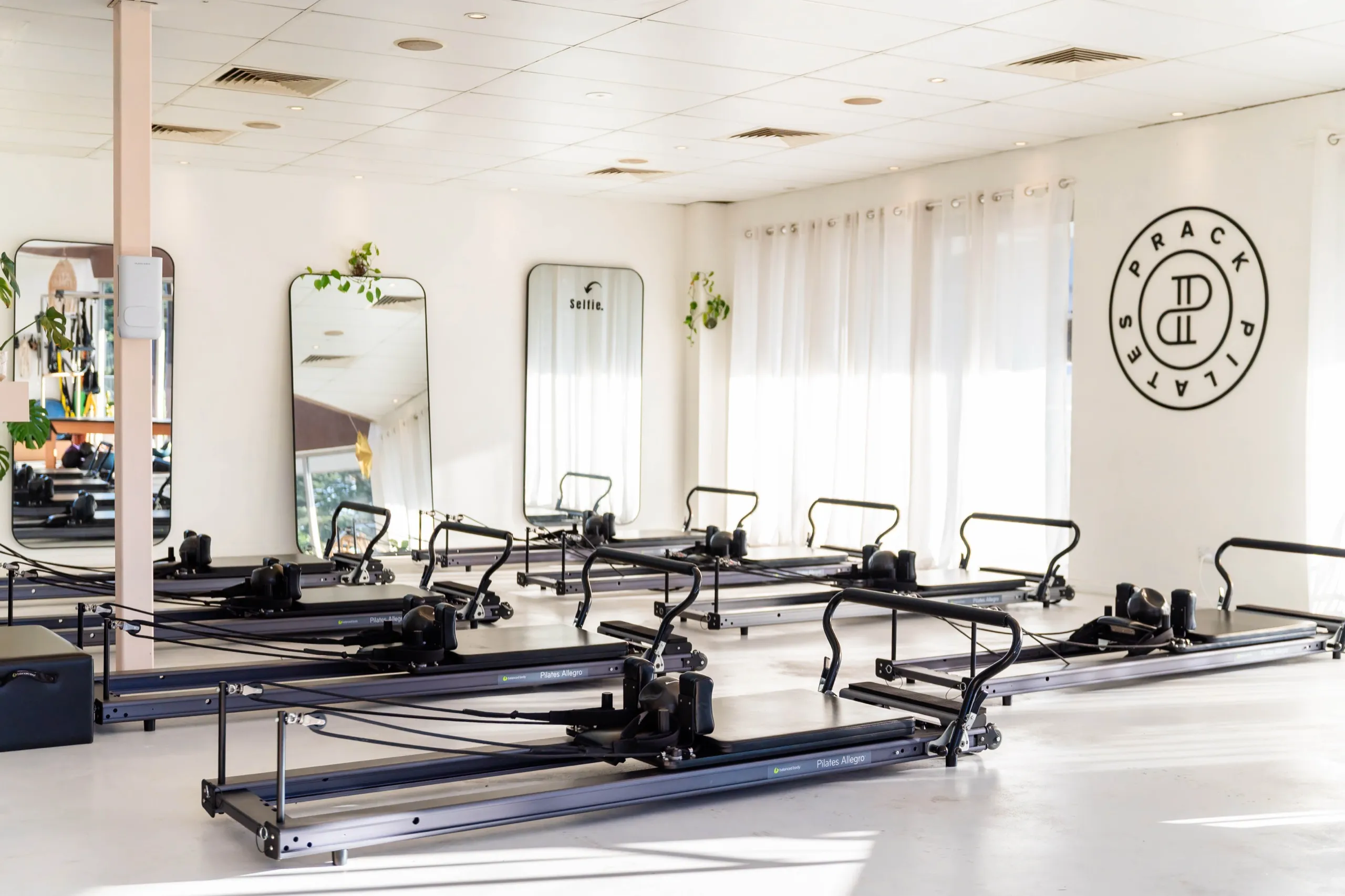 The main room at Prack Pilates: Reformers facing the wall with the Prack Pilates badge, sheer curtains and mirrors.